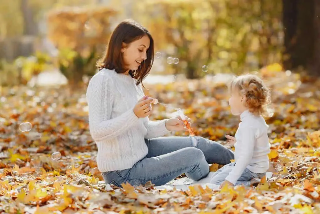 Happy young mother IN JEANS and little daughter having fun in autumn park