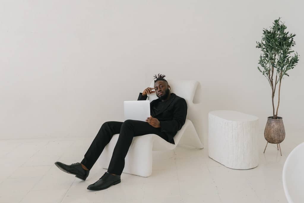 Tall Man in Black Suit Seated on a White Chair